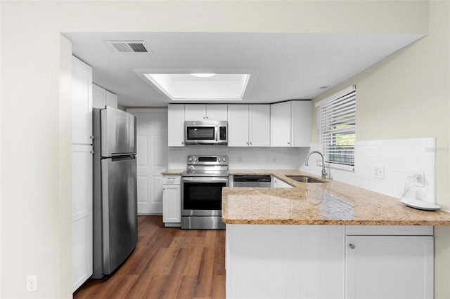 kitchen featuring decorative backsplash, white cabinets, appliances with stainless steel finishes, a peninsula, and a sink