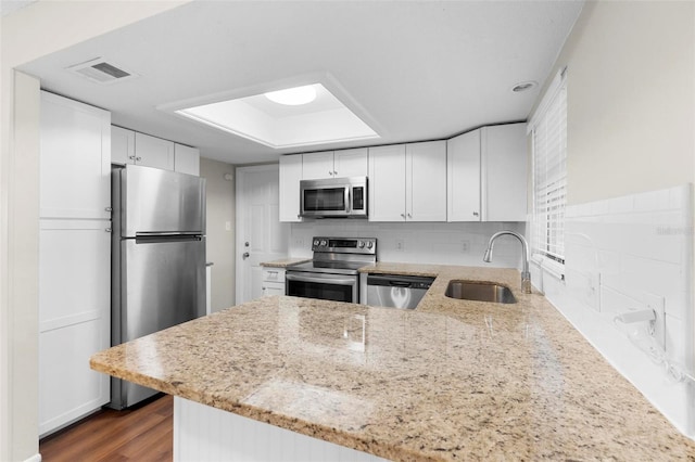 kitchen featuring a peninsula, appliances with stainless steel finishes, a sink, and light stone countertops