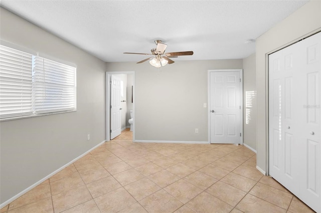 unfurnished bedroom featuring a textured ceiling, a closet, light tile patterned flooring, and baseboards