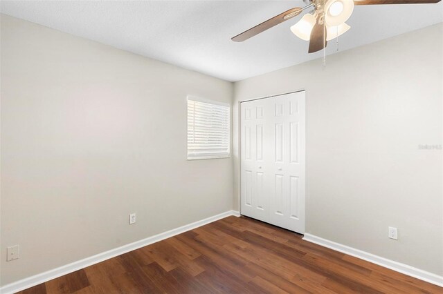 unfurnished bedroom with a closet, dark wood-style flooring, ceiling fan, and baseboards