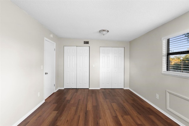 unfurnished bedroom featuring dark wood finished floors, two closets, visible vents, and baseboards