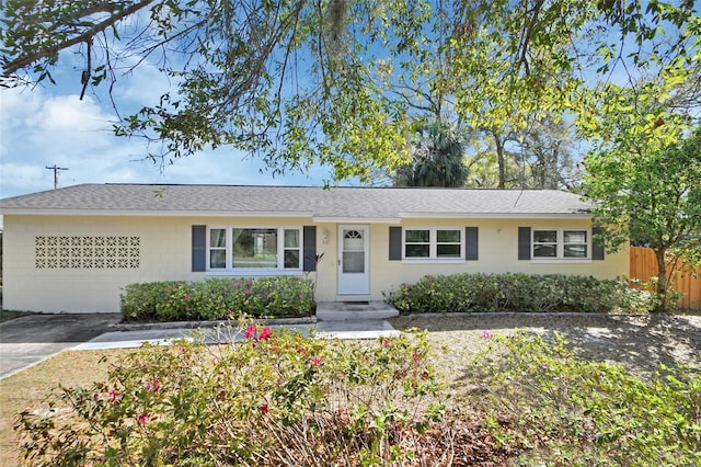 ranch-style house with fence, concrete driveway, and roof with shingles