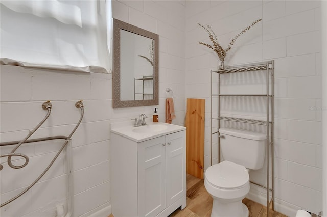 bathroom featuring toilet, wood finished floors, tile walls, and vanity