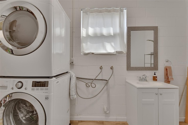 clothes washing area featuring stacked washer and clothes dryer, a sink, tile walls, and laundry area