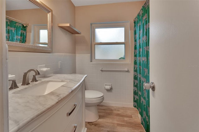 full bath featuring toilet, wood finished floors, vanity, tile walls, and wainscoting