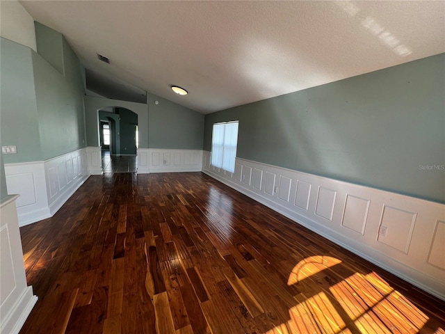 spare room with arched walkways, lofted ceiling, a wainscoted wall, visible vents, and hardwood / wood-style floors