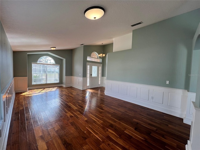 empty room featuring vaulted ceiling, a textured ceiling, wainscoting, and wood finished floors