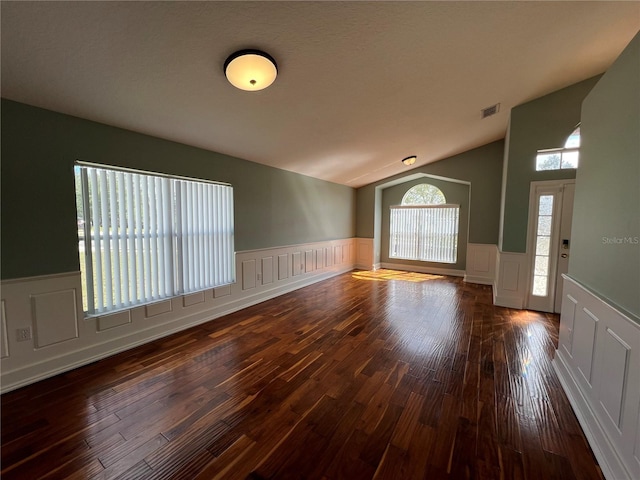 interior space featuring vaulted ceiling, a wainscoted wall, wood-type flooring, and visible vents