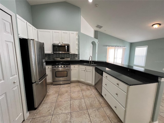 kitchen with stainless steel appliances, a peninsula, a sink, vaulted ceiling, and dark countertops