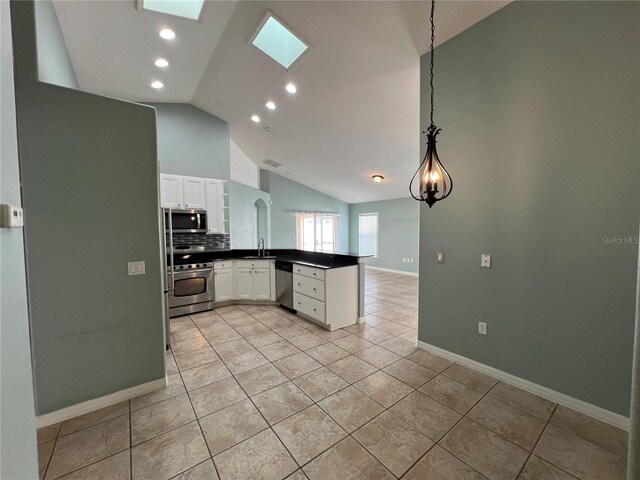 kitchen with stainless steel appliances, a peninsula, a sink, white cabinetry, and dark countertops