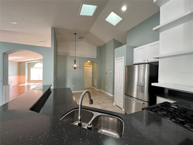 kitchen with arched walkways, white cabinets, vaulted ceiling, a sink, and stainless steel fridge