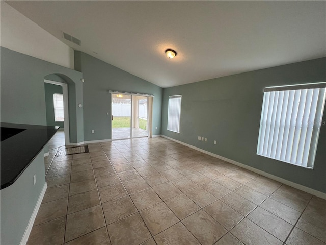 tiled empty room featuring lofted ceiling, arched walkways, visible vents, and baseboards