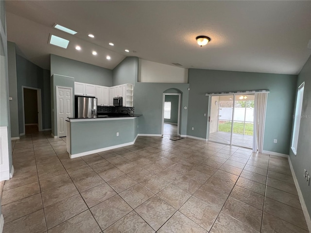 kitchen featuring arched walkways, stainless steel appliances, white cabinetry, open floor plan, and dark countertops