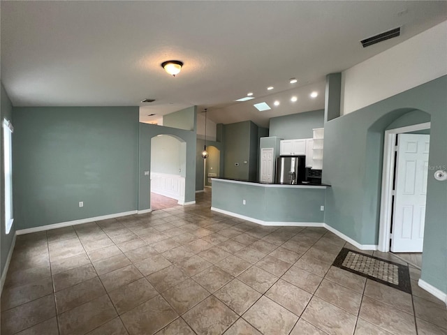 empty room featuring baseboards, visible vents, arched walkways, lofted ceiling, and tile patterned flooring