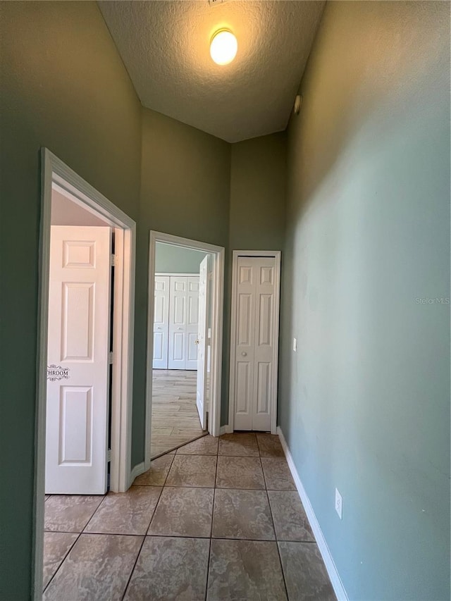 corridor with tile patterned flooring, a textured ceiling, and baseboards