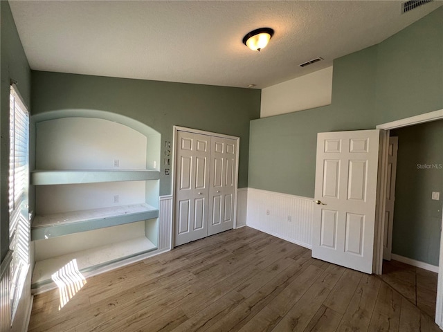 unfurnished bedroom with visible vents, a closet, wainscoting, and hardwood / wood-style flooring