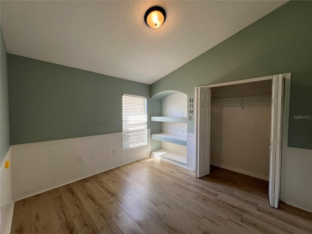 unfurnished bedroom featuring lofted ceiling, a closet, wainscoting, and wood finished floors