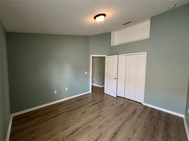 unfurnished bedroom with lofted ceiling, wood finished floors, visible vents, baseboards, and a closet