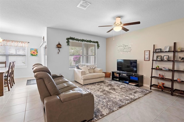 living room with ceiling fan, a textured ceiling, light tile patterned flooring, and visible vents