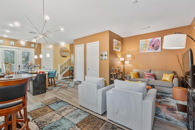 living area with a notable chandelier, visible vents, stairs, french doors, and light wood-type flooring