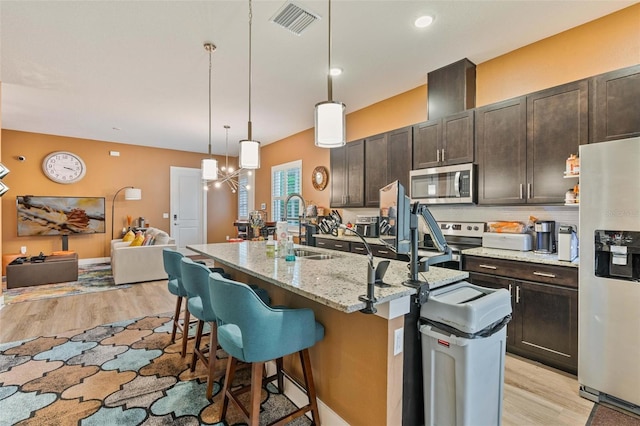 kitchen featuring dark brown cabinetry, visible vents, appliances with stainless steel finishes, a breakfast bar, and open floor plan