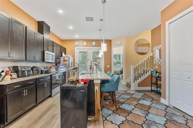 kitchen featuring a sink, visible vents, light wood-style floors, appliances with stainless steel finishes, and a kitchen bar