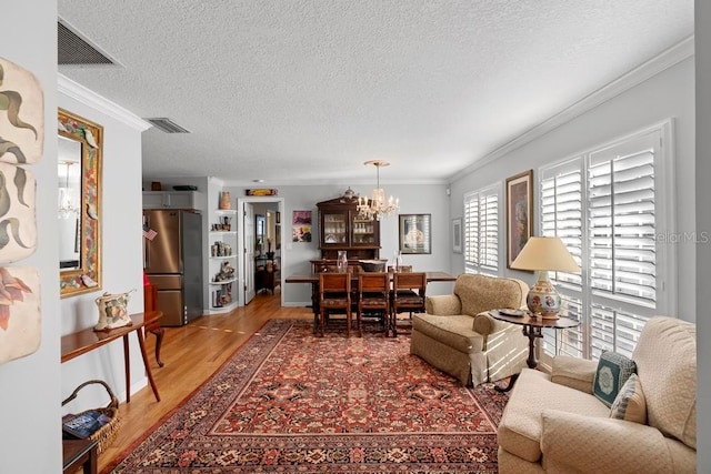 living room with a chandelier, light wood-type flooring, visible vents, and crown molding