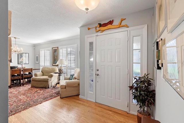 foyer entrance featuring an inviting chandelier, light wood-style flooring, crown molding, and a textured ceiling