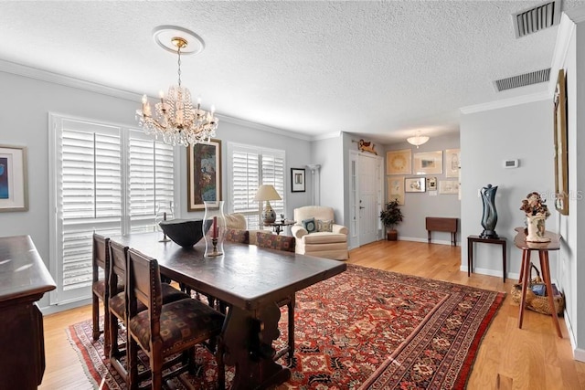 dining space featuring ornamental molding, visible vents, light wood-style flooring, and a textured ceiling