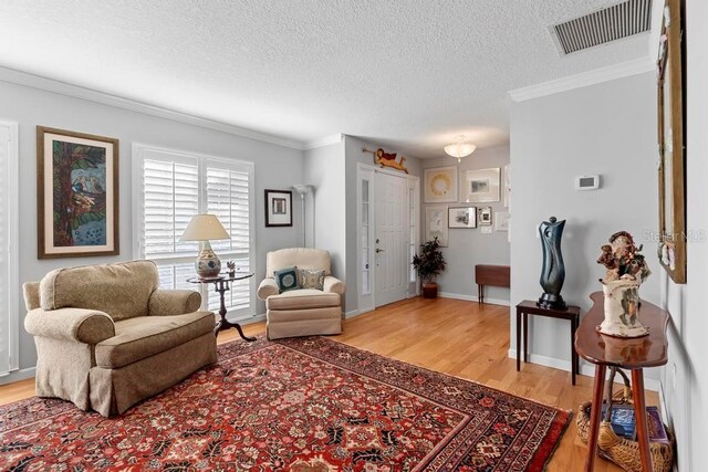 interior space with ornamental molding, visible vents, light wood-style flooring, and a textured ceiling