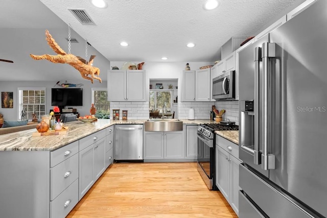 kitchen featuring visible vents, appliances with stainless steel finishes, a peninsula, light wood-type flooring, and a sink