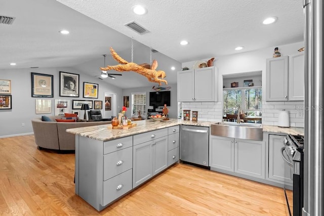 kitchen featuring light wood-style flooring, appliances with stainless steel finishes, a peninsula, vaulted ceiling, and a sink