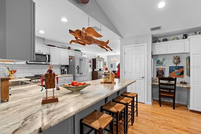 kitchen with appliances with stainless steel finishes, a breakfast bar area, a peninsula, vaulted ceiling, and light wood-type flooring