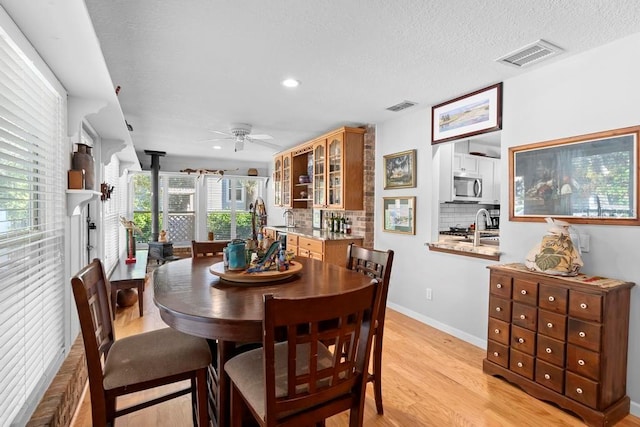 dining room featuring a wood stove, light wood-type flooring, visible vents, and a ceiling fan