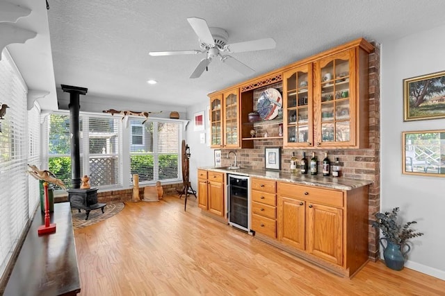 bar with wine cooler, light wood-style floors, a wood stove, a sink, and wet bar