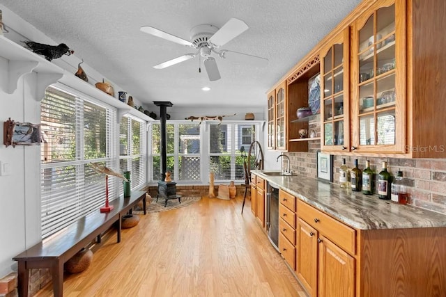 kitchen featuring a sink, light wood-style floors, backsplash, brown cabinets, and a wood stove