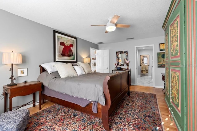 bedroom with a textured ceiling, visible vents, a ceiling fan, baseboards, and light wood-type flooring