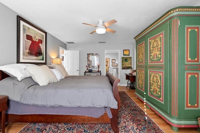 bedroom featuring a textured ceiling, wood finished floors, visible vents, and a ceiling fan