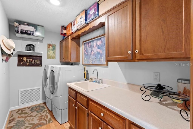 washroom featuring cabinet space, baseboards, visible vents, washing machine and clothes dryer, and a sink