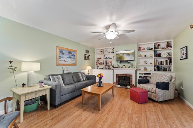 living room featuring light wood finished floors, baseboards, a ceiling fan, a textured ceiling, and a brick fireplace