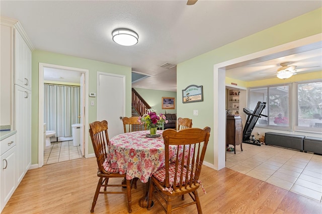 dining room featuring light wood-type flooring, ceiling fan, stairs, and visible vents