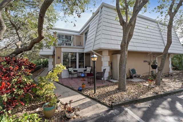 back of house with a balcony, stucco siding, mansard roof, and a patio