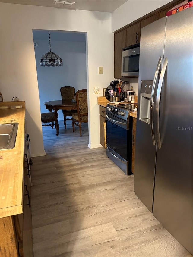 kitchen featuring butcher block counters, decorative light fixtures, light hardwood / wood-style floors, stainless steel appliances, and dark brown cabinets