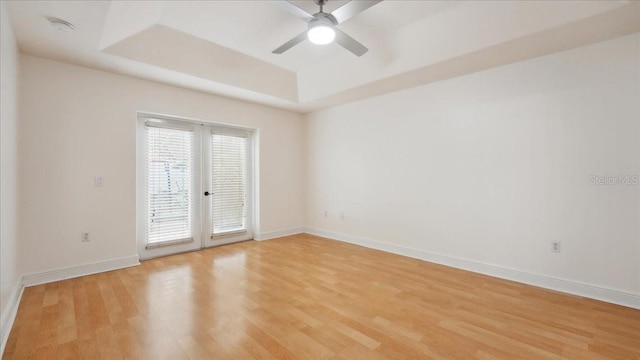 spare room featuring a tray ceiling, light hardwood / wood-style flooring, french doors, and ceiling fan