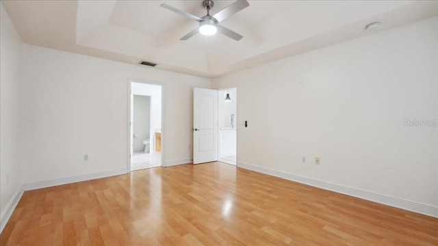 unfurnished bedroom with a tray ceiling, light wood-type flooring, ceiling fan, and ensuite bath