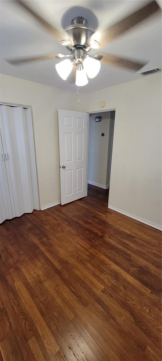 unfurnished bedroom with dark wood-style floors, a ceiling fan, visible vents, and baseboards