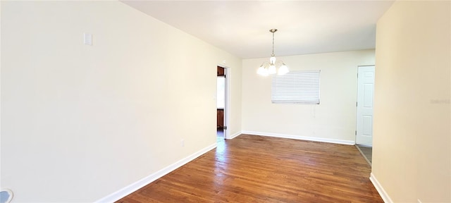 unfurnished dining area featuring an inviting chandelier, dark wood finished floors, and baseboards