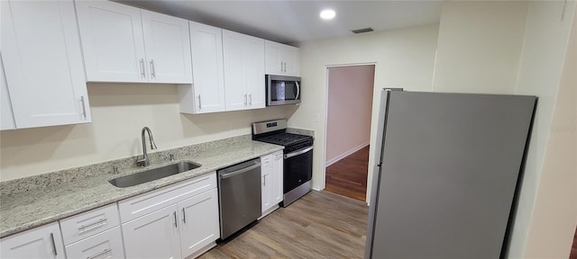 kitchen featuring visible vents, white cabinets, light stone counters, appliances with stainless steel finishes, and a sink