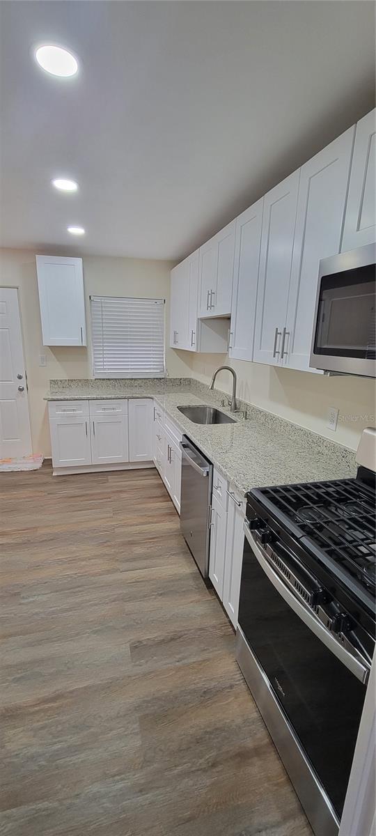 kitchen featuring light stone countertops, white cabinetry, appliances with stainless steel finishes, and a sink