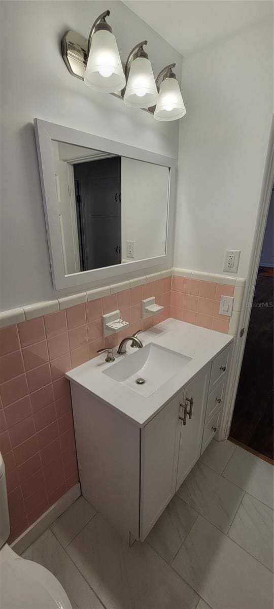 bathroom with toilet, vanity, tile walls, marble finish floor, and wainscoting